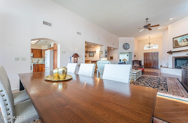 dining space with high vaulted ceiling, ceiling fan with notable chandelier, wood-type flooring, and a tile fireplace