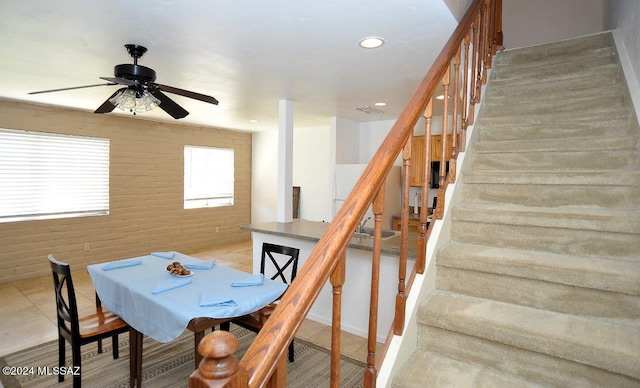 dining area featuring ceiling fan and brick wall