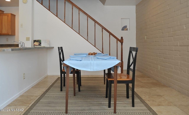 dining room featuring light tile patterned floors, sink, and brick wall