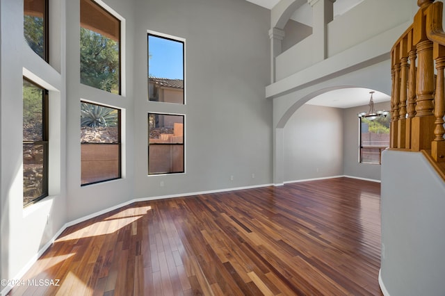 unfurnished living room featuring a notable chandelier, wood-type flooring, and a towering ceiling