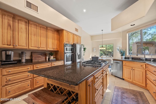 kitchen featuring hanging light fixtures, stainless steel appliances, dark stone countertops, a center island, and a breakfast bar