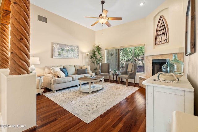 living room featuring ceiling fan, a towering ceiling, a fireplace, and dark hardwood / wood-style floors