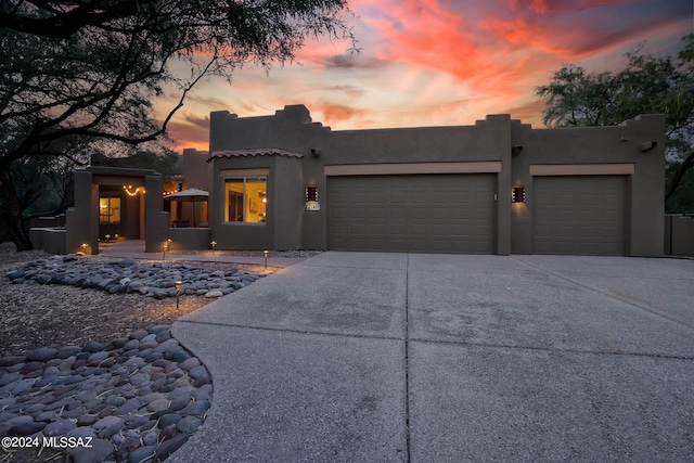 pueblo-style home with a garage, driveway, and stucco siding