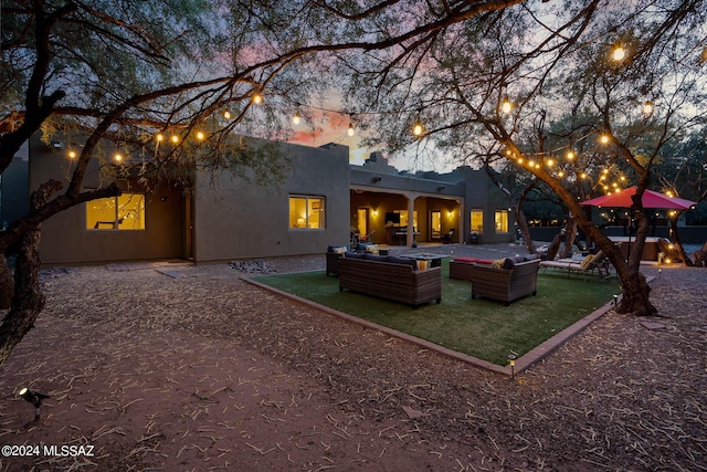 back house at dusk with an outdoor living space and a patio