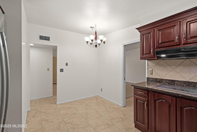 kitchen featuring pendant lighting, stovetop, decorative backsplash, dark stone counters, and a chandelier