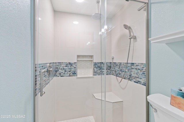 bathroom with toilet, a shower stall, and a textured wall