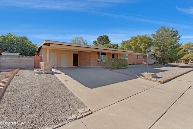 ranch-style home featuring a carport, driveway, brick siding, and fence