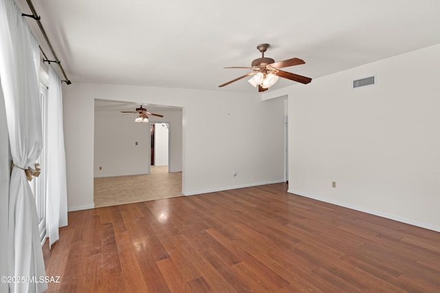 unfurnished room with a ceiling fan, wood finished floors, visible vents, and baseboards