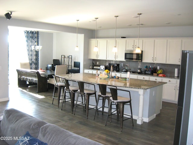 kitchen with a center island with sink, white cabinets, hanging light fixtures, and appliances with stainless steel finishes