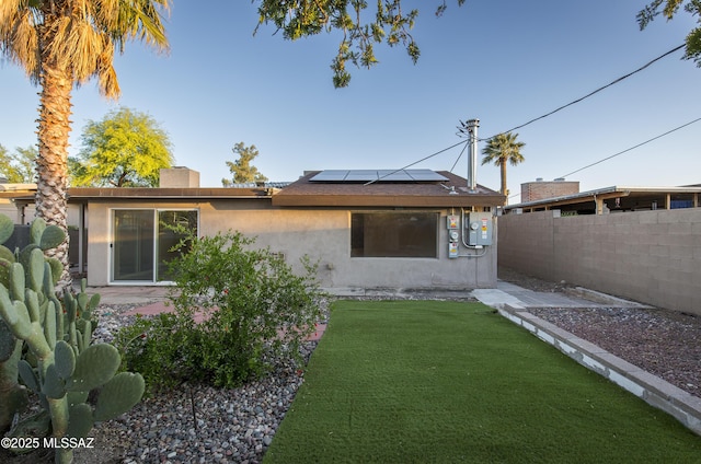 back of property with solar panels and a lawn