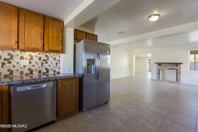 kitchen featuring backsplash, dark stone countertops, light tile patterned floors, and stainless steel appliances