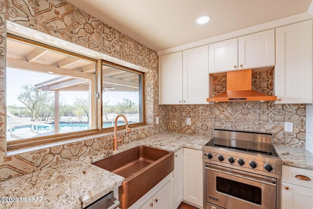 kitchen with white cabinetry, light stone countertops, wall chimney range hood, and premium stove