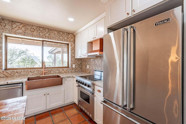 kitchen featuring light stone countertops, white cabinets, premium appliances, and sink