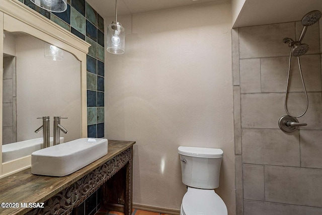 bathroom with toilet, tiled shower, and sink