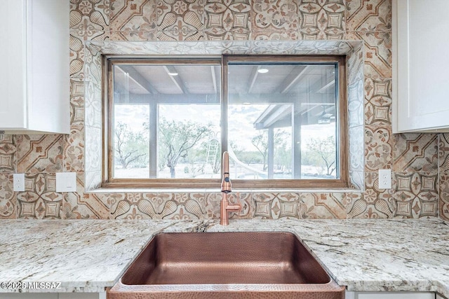 interior details featuring decorative backsplash, sink, light stone counters, and white cabinetry