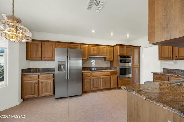 kitchen with dark stone counters, decorative light fixtures, light tile patterned flooring, stainless steel appliances, and a chandelier