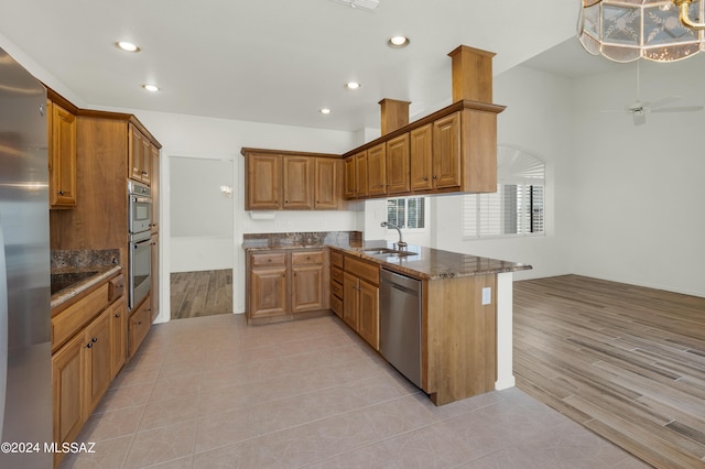 kitchen with kitchen peninsula, stainless steel appliances, ceiling fan, sink, and dark stone countertops