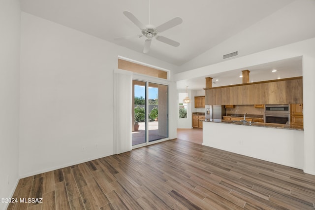 kitchen featuring dark stone counters, stainless steel appliances, ceiling fan, sink, and high vaulted ceiling