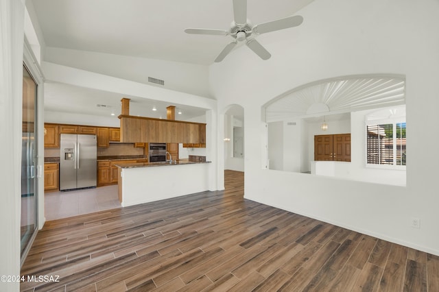 kitchen featuring kitchen peninsula, stainless steel refrigerator with ice dispenser, dark stone counters, multiple ovens, and ceiling fan