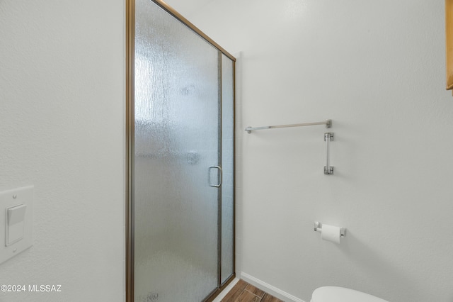 bathroom featuring wood-type flooring, toilet, and a shower with shower door