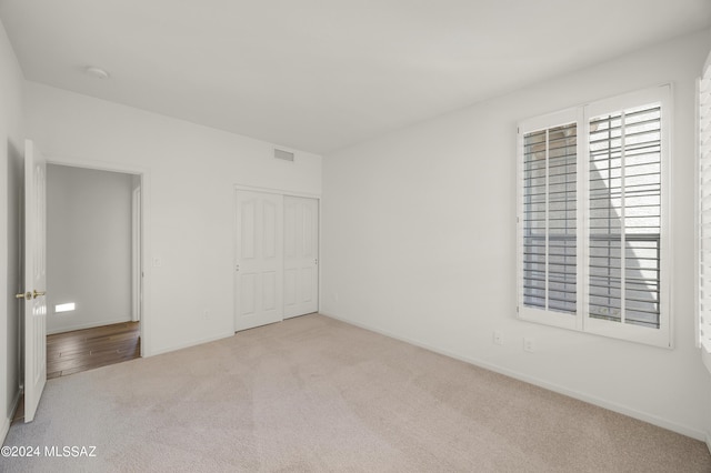 unfurnished bedroom with multiple windows, light carpet, and a closet