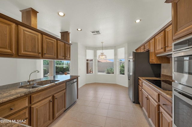 kitchen featuring stainless steel appliances, a healthy amount of sunlight, sink, dark stone countertops, and light tile patterned flooring