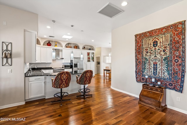 kitchen featuring hanging light fixtures, wall chimney exhaust hood, dark hardwood / wood-style floors, white cabinetry, and stainless steel appliances