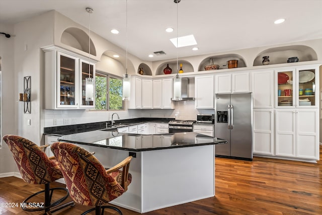 kitchen with a skylight, white cabinetry, wall chimney range hood, pendant lighting, and appliances with stainless steel finishes