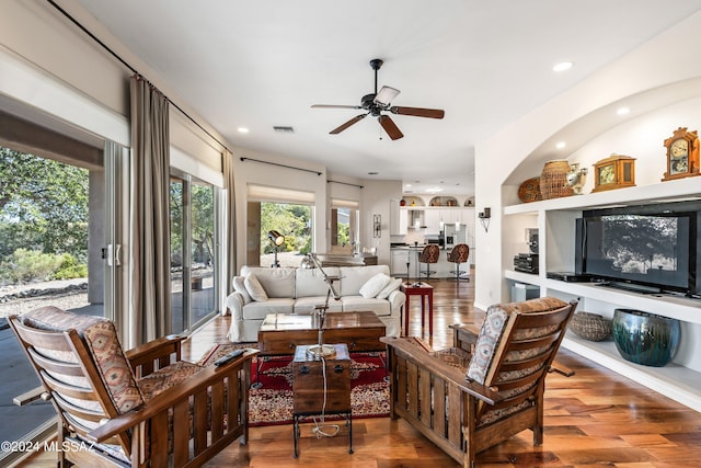 living room featuring built in shelves, ceiling fan, and wood-type flooring