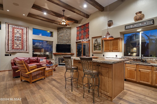 kitchen featuring a stone fireplace, a kitchen breakfast bar, light wood-type flooring, hanging light fixtures, and sink