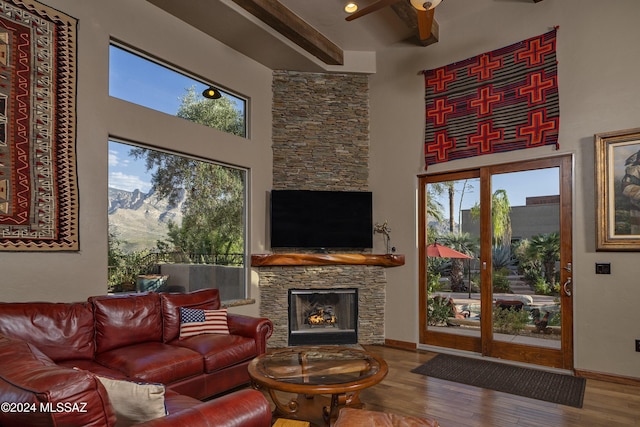 living room with ceiling fan, a fireplace, beam ceiling, a high ceiling, and hardwood / wood-style flooring