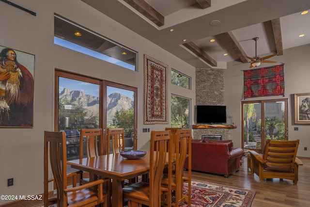 dining area with ceiling fan, light wood-type flooring, a fireplace, french doors, and beamed ceiling