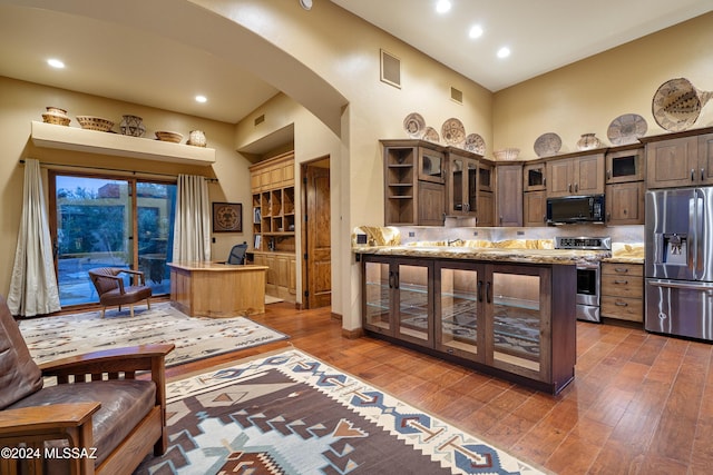 kitchen with light stone counters, dark brown cabinetry, appliances with stainless steel finishes, and a towering ceiling