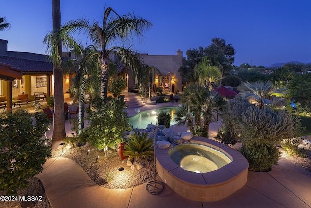 pool at dusk featuring a patio and an in ground hot tub