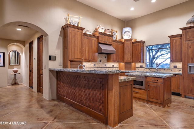 kitchen with sink, backsplash, dark stone counters, and a center island