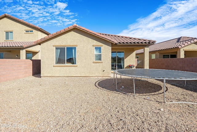 rear view of property featuring stucco siding, a fenced backyard, a tiled roof, and a trampoline