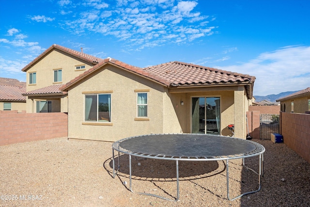 rear view of property featuring a trampoline, a fenced backyard, a tiled roof, and stucco siding
