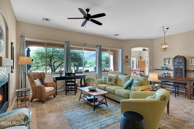 tiled living room with a tile fireplace and ceiling fan with notable chandelier