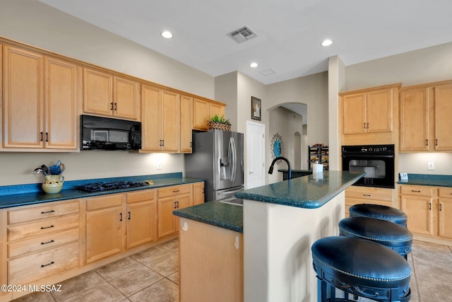 kitchen with a kitchen bar, a kitchen island with sink, black appliances, light brown cabinets, and light tile patterned flooring