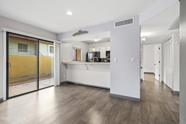 kitchen with kitchen peninsula, dark hardwood / wood-style flooring, white cabinetry, black appliances, and decorative backsplash