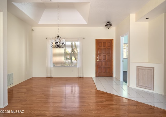entryway featuring light wood-style floors, a raised ceiling, a notable chandelier, and visible vents