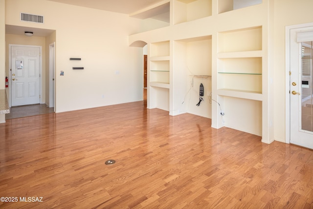 unfurnished living room featuring visible vents, built in shelves, and wood finished floors