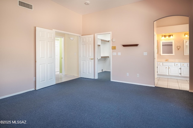 unfurnished bedroom featuring visible vents, light colored carpet, arched walkways, light tile patterned floors, and a spacious closet