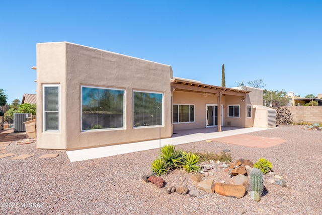 back of house with a storage unit, stucco siding, an outbuilding, central air condition unit, and a ceiling fan
