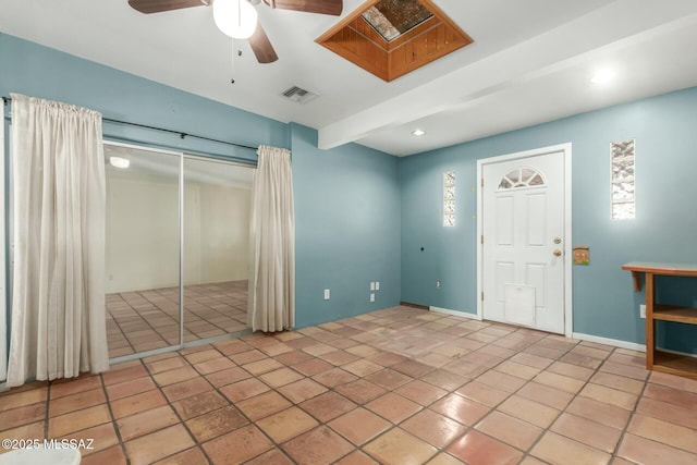 empty room with ceiling fan, beamed ceiling, a healthy amount of sunlight, and light tile patterned floors