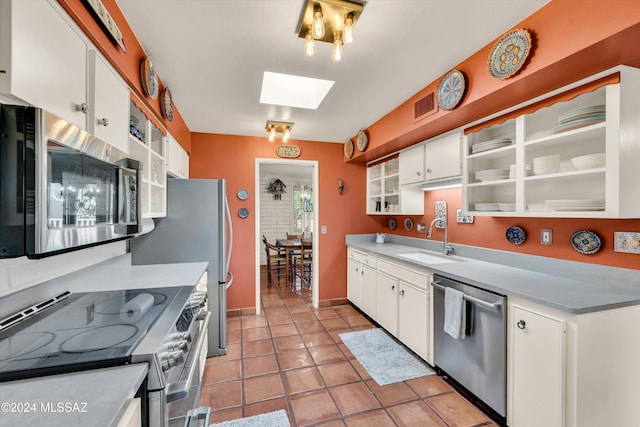 kitchen with appliances with stainless steel finishes, a skylight, sink, white cabinetry, and light tile patterned flooring