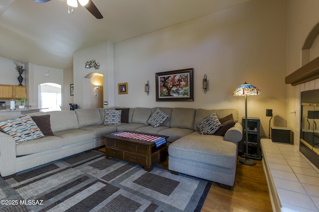 living area with wood finished floors, arched walkways, high vaulted ceiling, and ceiling fan