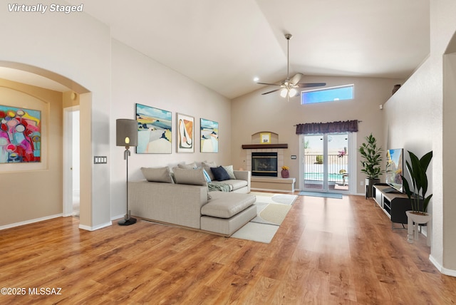 10187 E Watson Dr, Tucson, AZ 85730 - living room featuring a ceiling fan, arched walkways, light wood-type flooring, high vaulted ceiling, and a fireplace