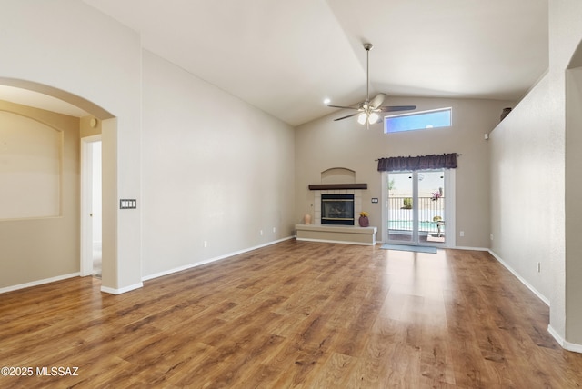 10187 E Watson Dr, Tucson, AZ 85730 - unfurnished living room featuring a ceiling fan, a tile fireplace, high vaulted ceiling, arched walkways, and wood finished floors