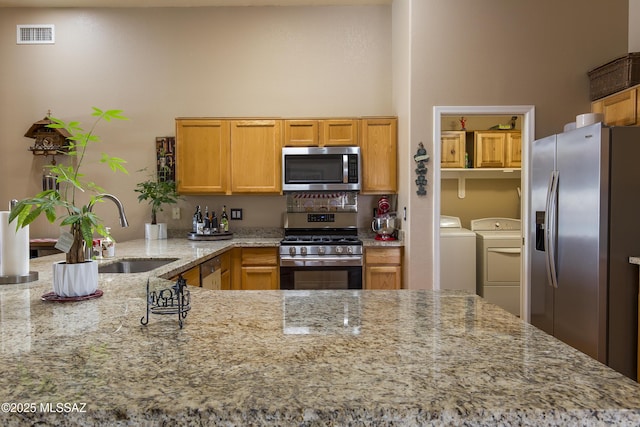 kitchen featuring visible vents, light stone countertops, washer and dryer, stainless steel appliances, and a sink